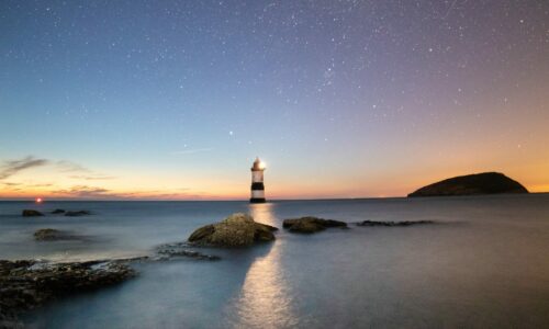 Océan avec avancée rocheuse et phare lumineux au crépuscule. Photographe : Neil Thomas.